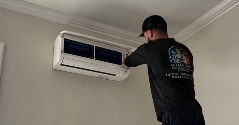 Jack Giuliani, owner, working on an ac wall unit in Giuliani Air Conditioning & Heating shirt